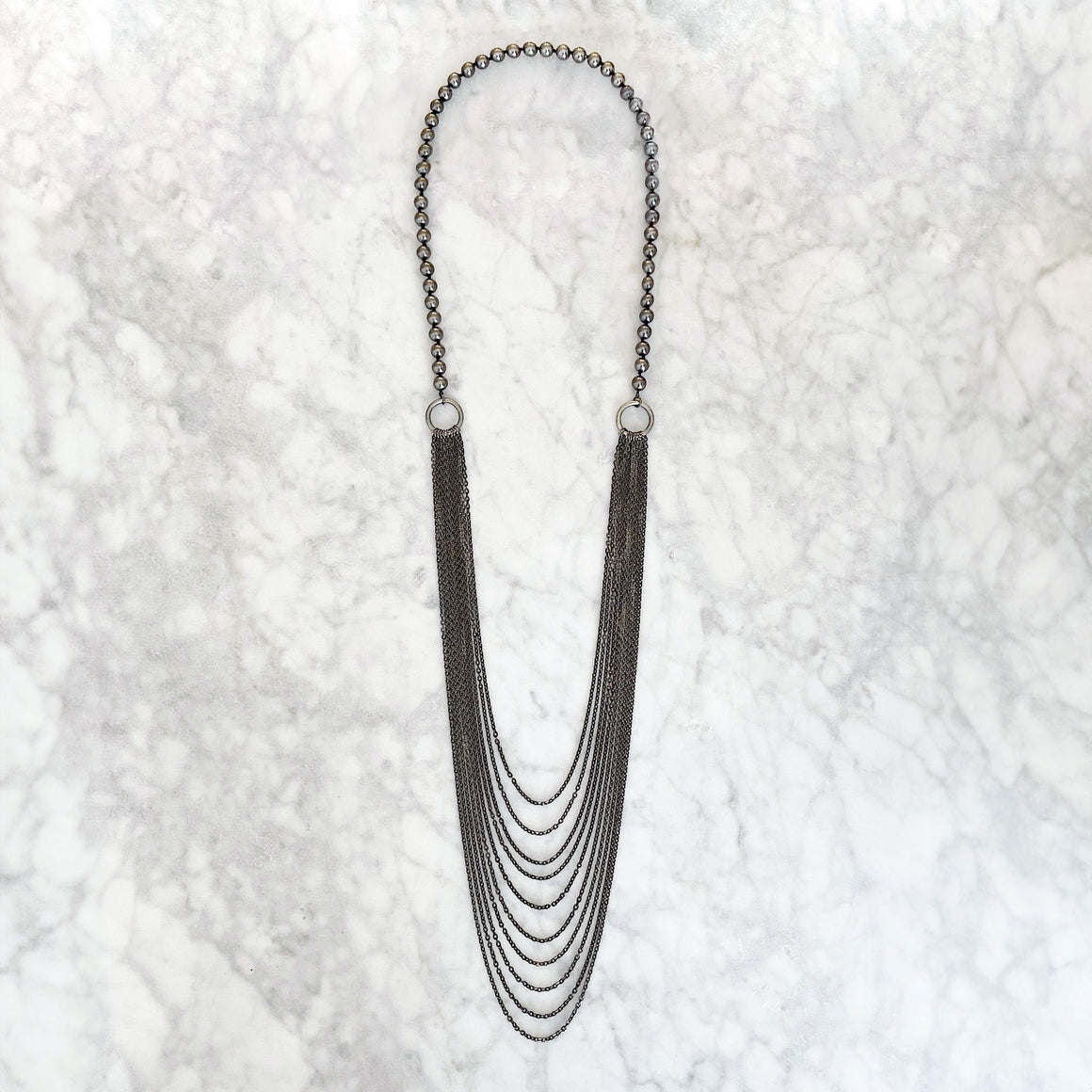 Model wearing a long grey bead necklace with cascading gunmetal-tone chain strands over a white blouse