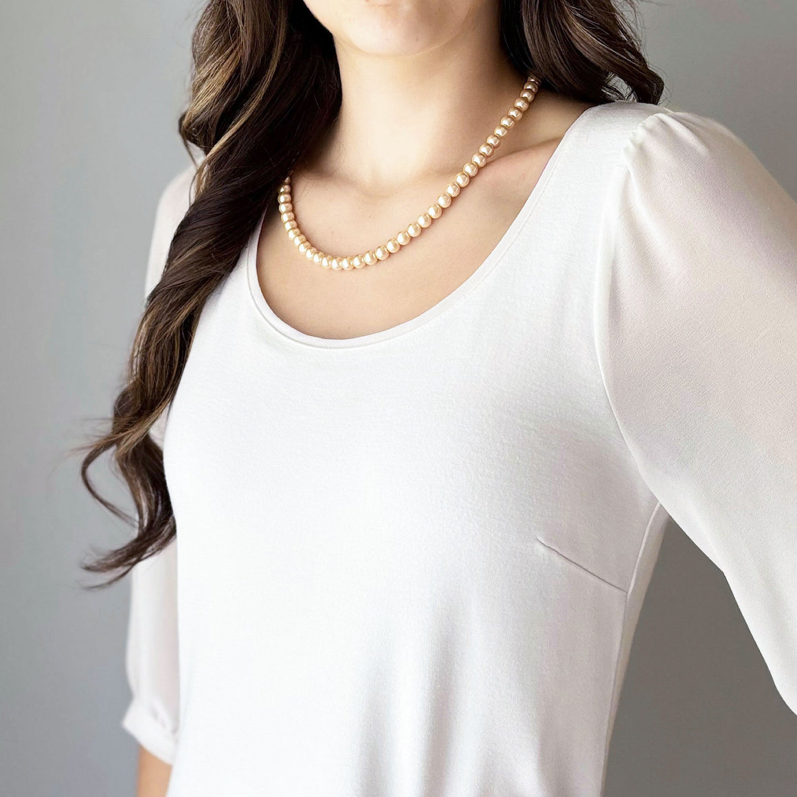 Blush peach glass pearl necklace arranged on white marble