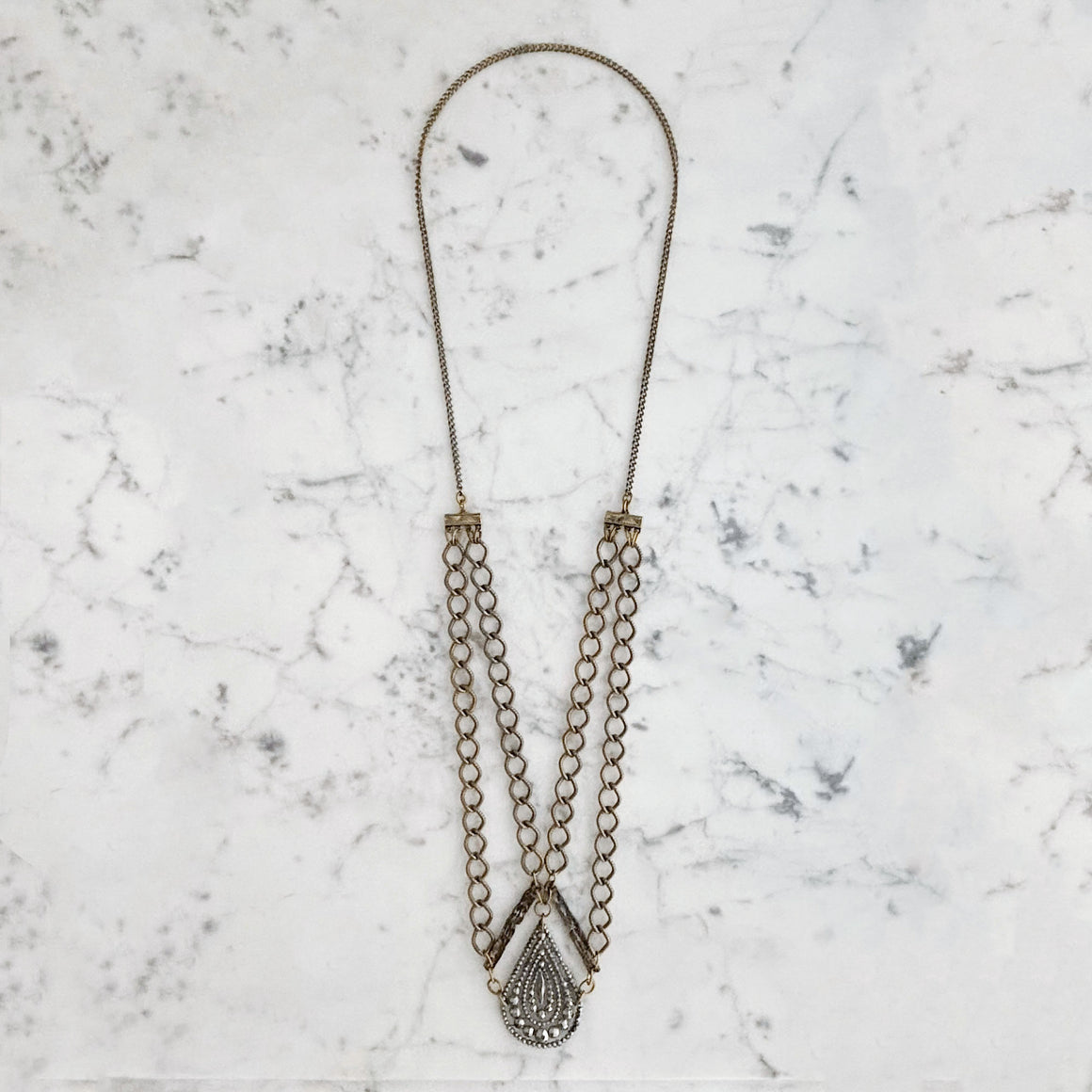 Close-up of a model wearing a long mixed metal necklace with layered oval links and an ornate teardrop pendant