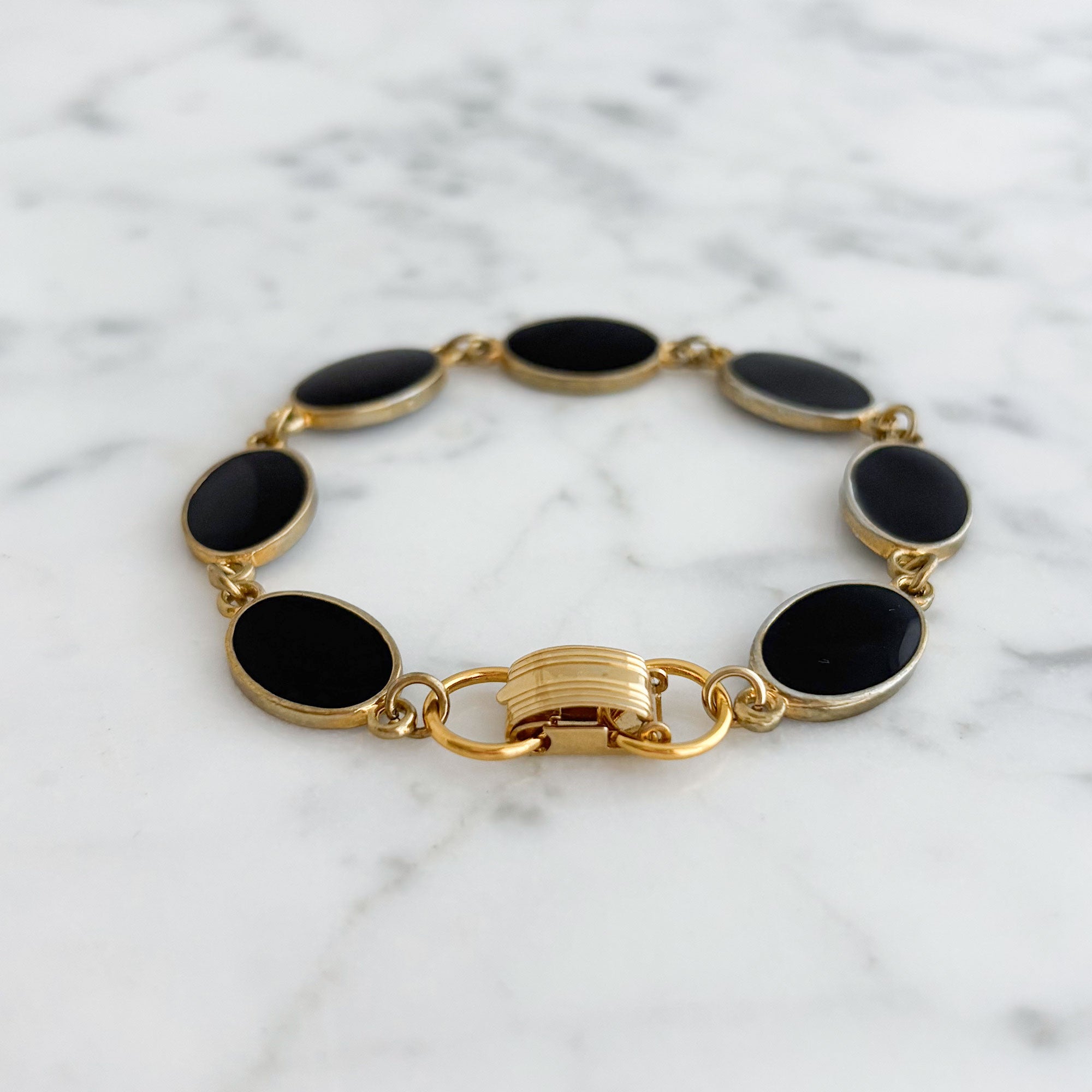 Gold-tone oval links with black enamel centres arranged in a bracelet on white marble