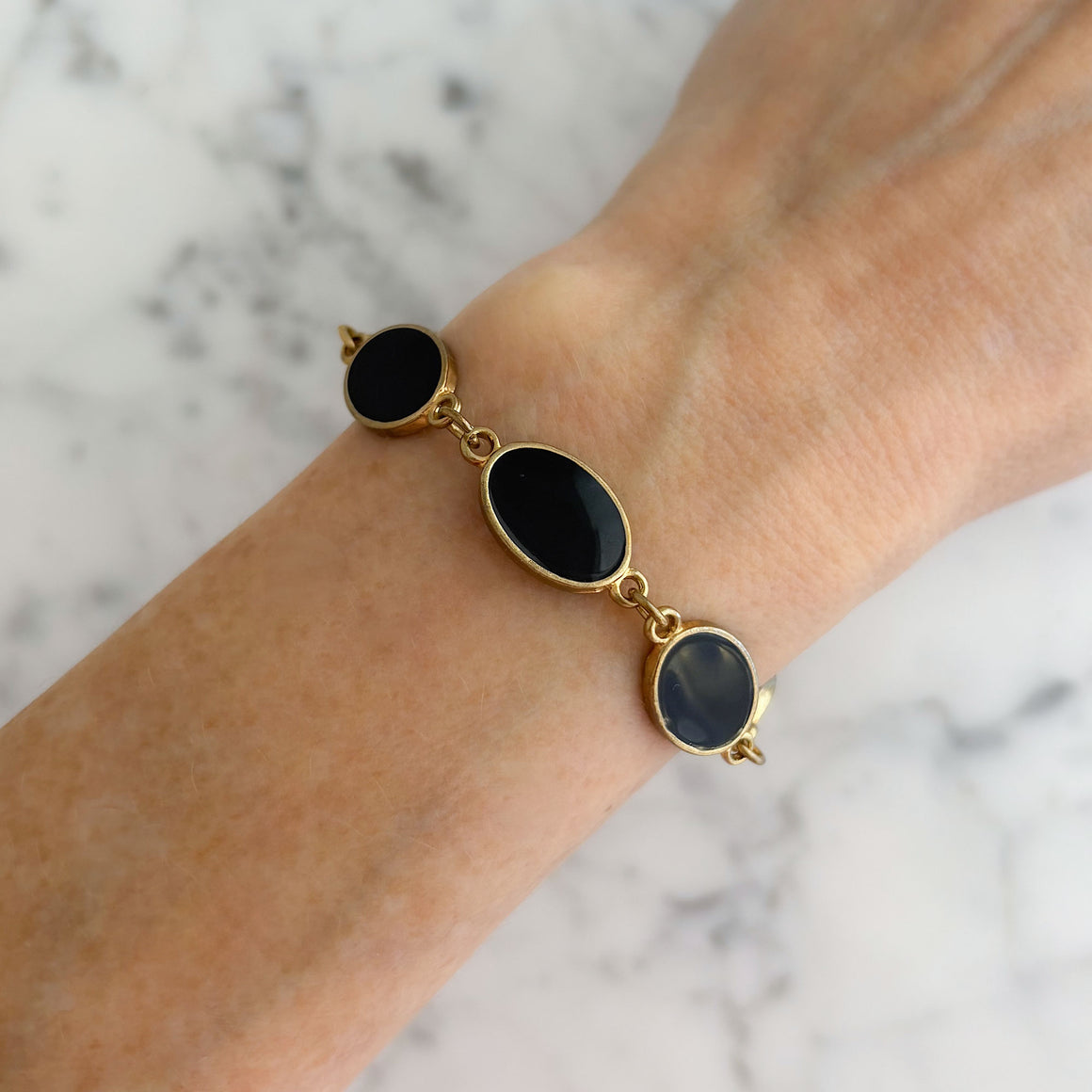 Gold-tone oval links with black enamel centres arranged in a bracelet on white marble
