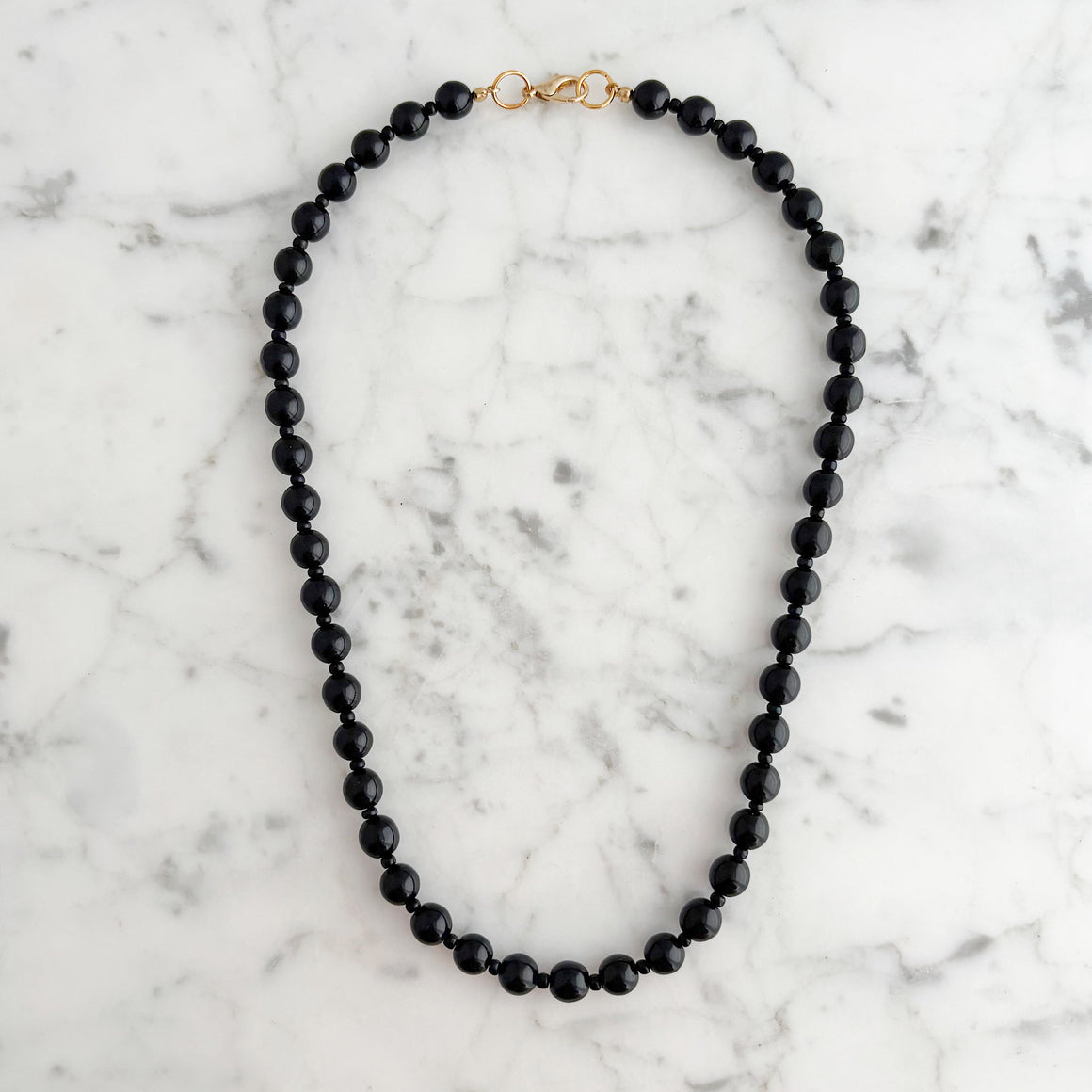 Model wearing a single strand of glossy black beads at the neckline of a white blouse