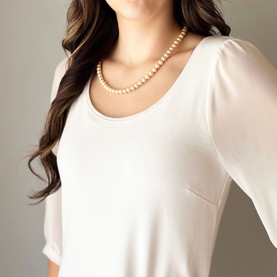 Blush peach glass pearl necklace arranged on white marble