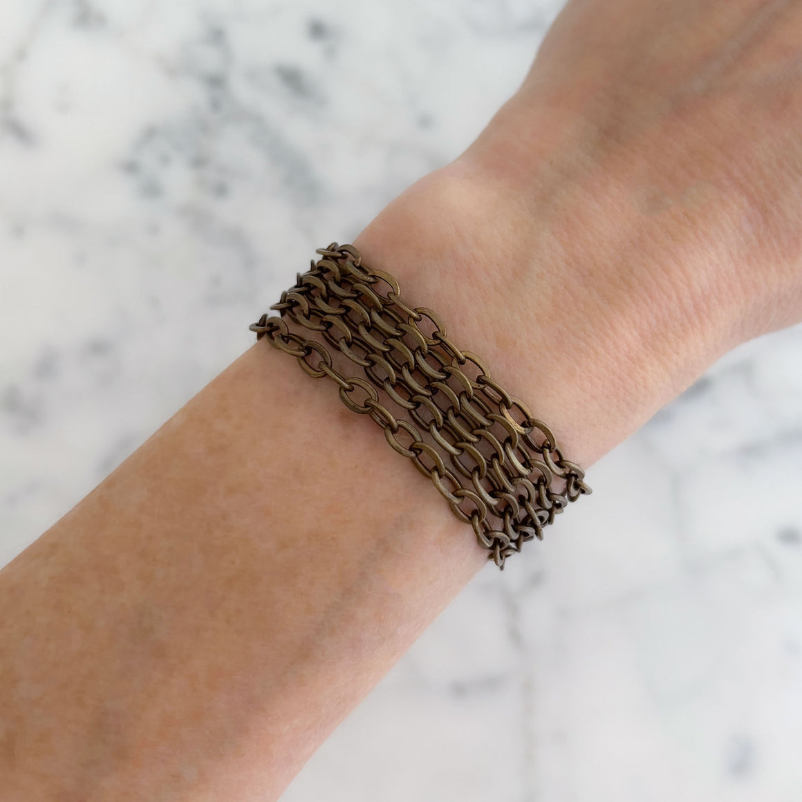 Brass tone layered chain bracelet with multiple cable-chain strands displayed on marble