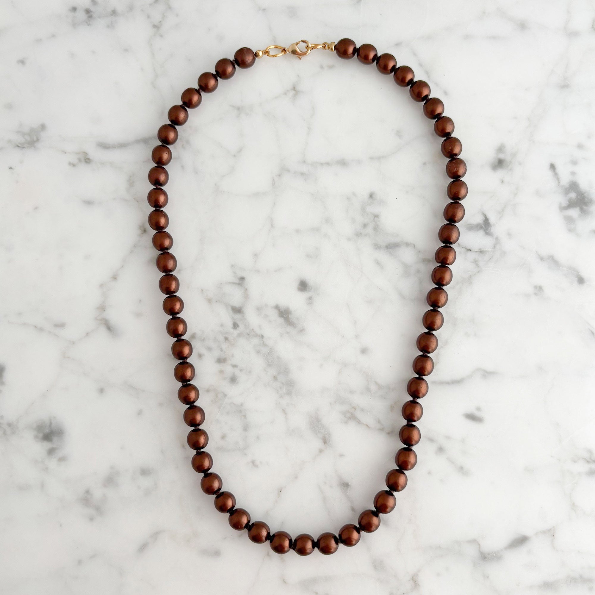 Full strand of rounded copper-coloured glass pearls arranged on white marble