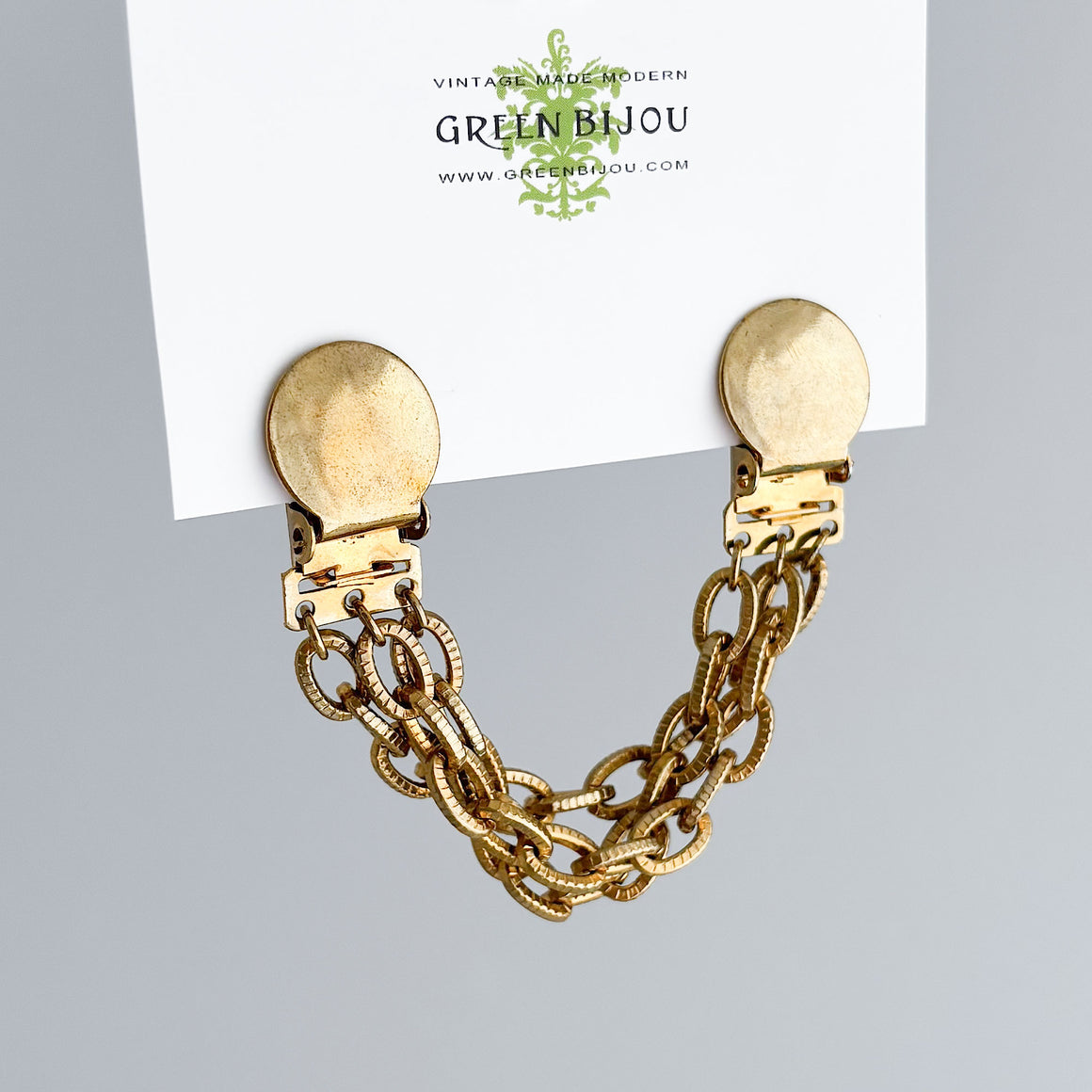 Gold-tone cardigan clips with round discs and ridged chains fastening a grey fur collar