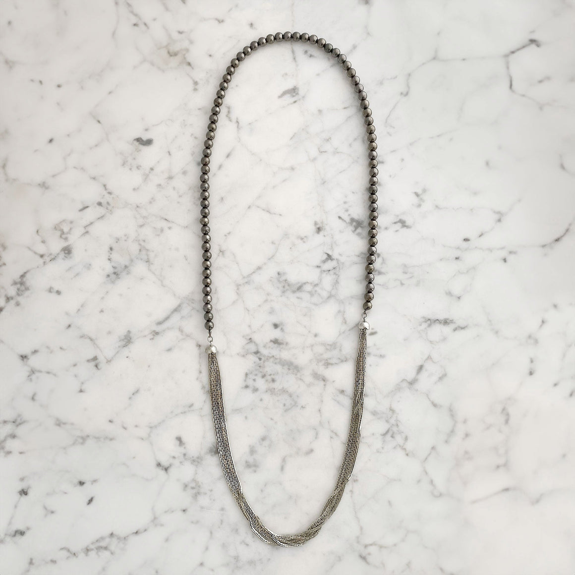 Model wearing a long multi-strand silver-tone necklace with dark hematite beads