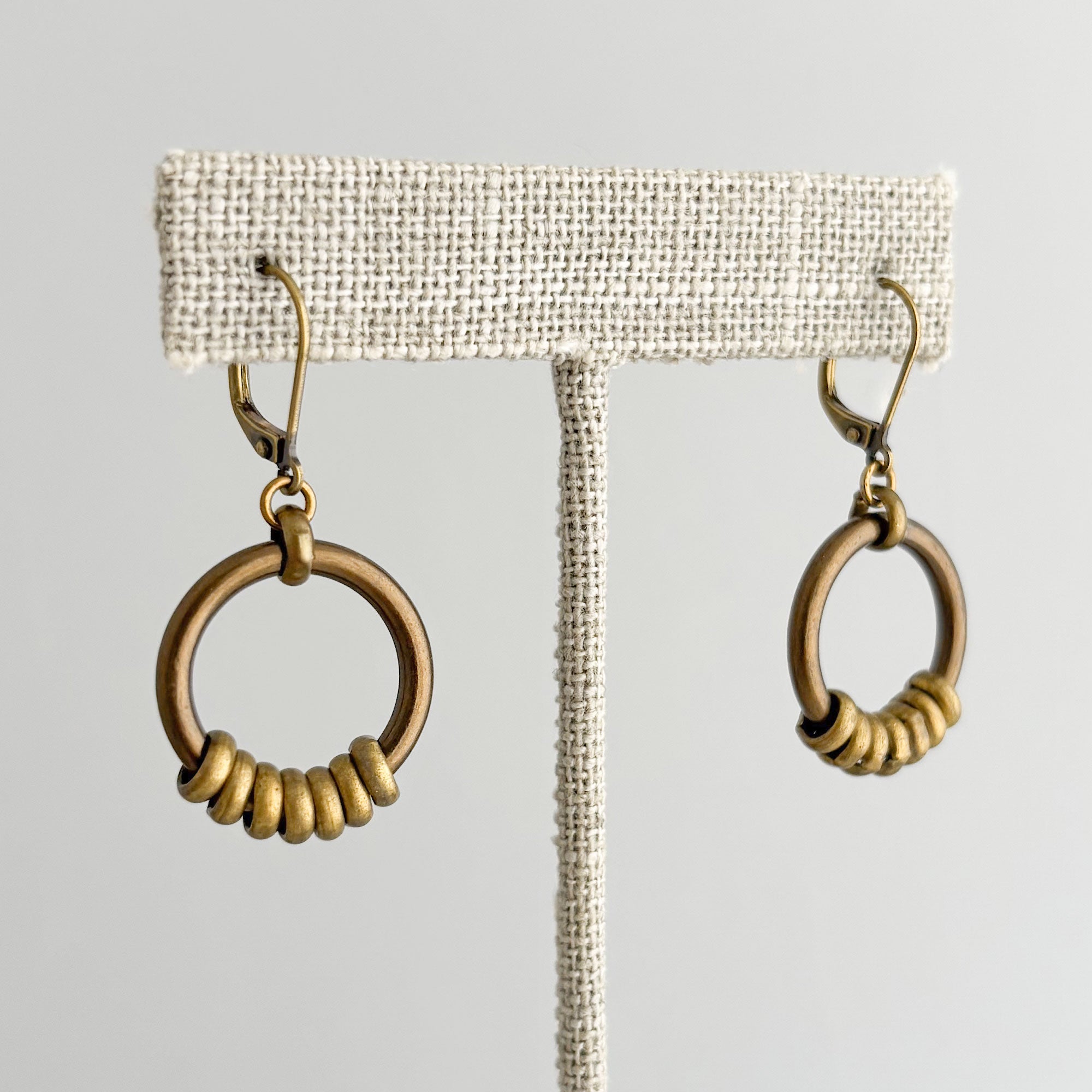 Oxidized brass-tone circular hoop earrings displayed on a linen t bar display