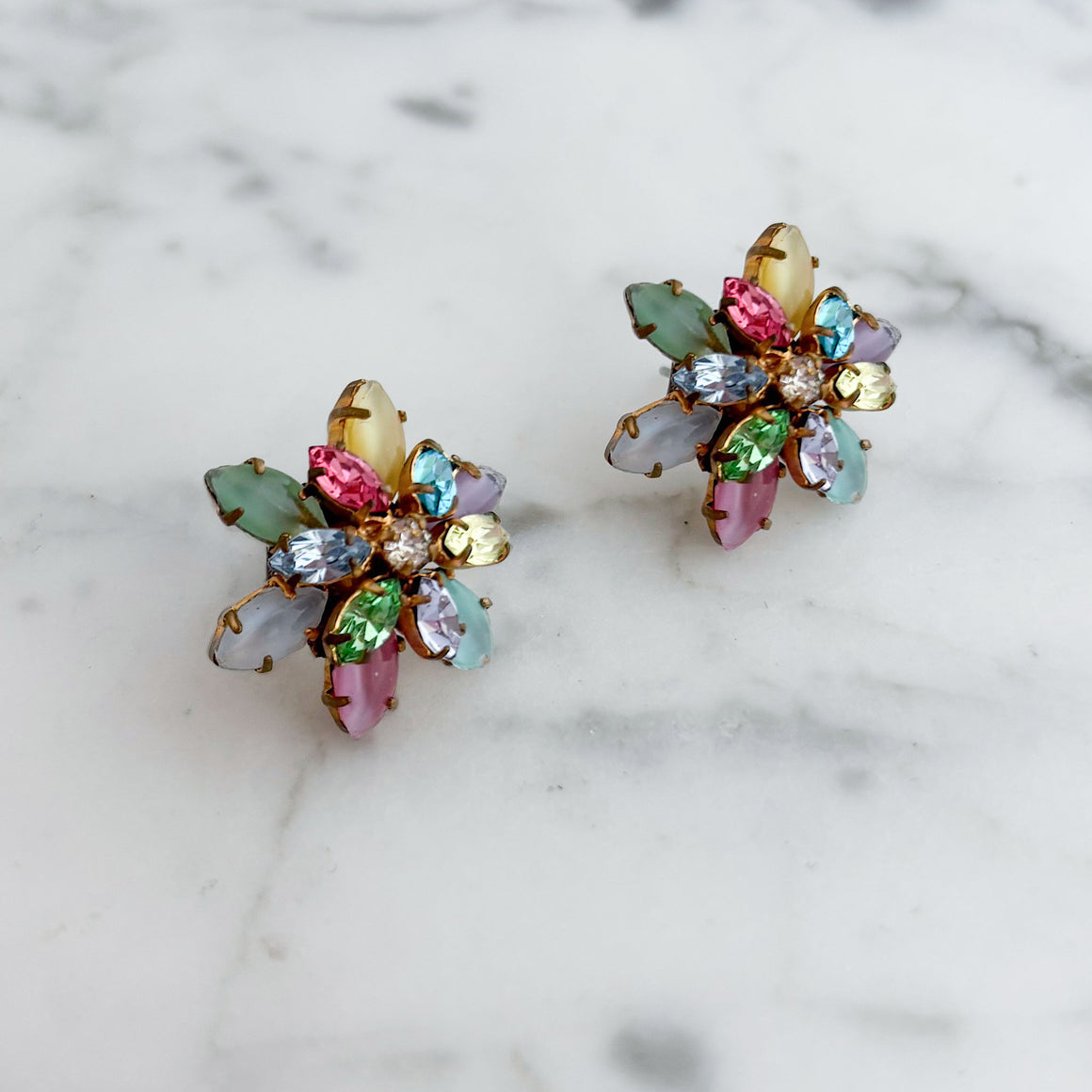 Close-up of a model wearing a colourful floral cluster stud earring with pastel rhinestones and a gold-tone setting