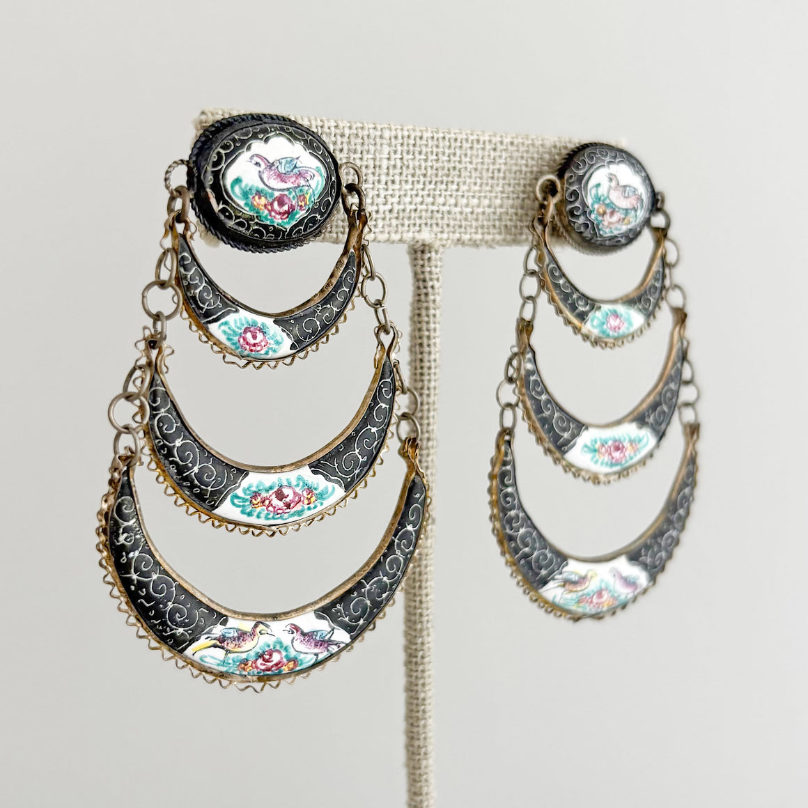 Close-up of a tiered enamel bird chandelier earring worn on the ear