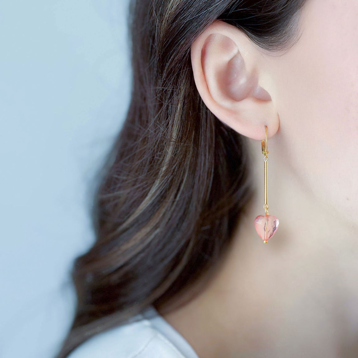 Pair of faceted translucent pink heart earrings with long gold-tone bars on white marble
