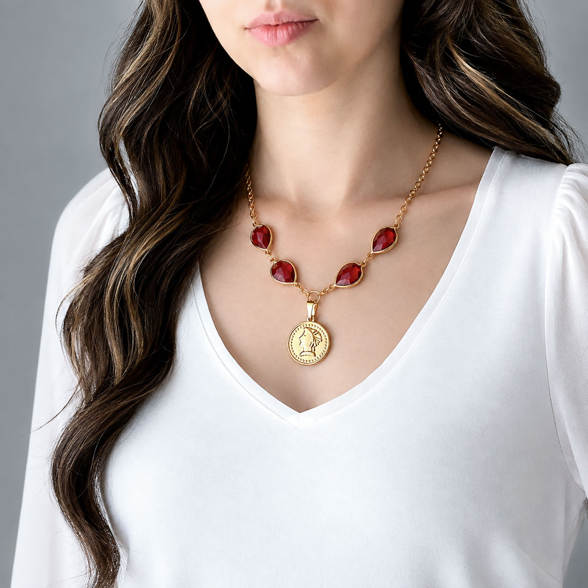 Vintage red crystal teardrop necklace with a gold-tone coin pendant displayed on marble