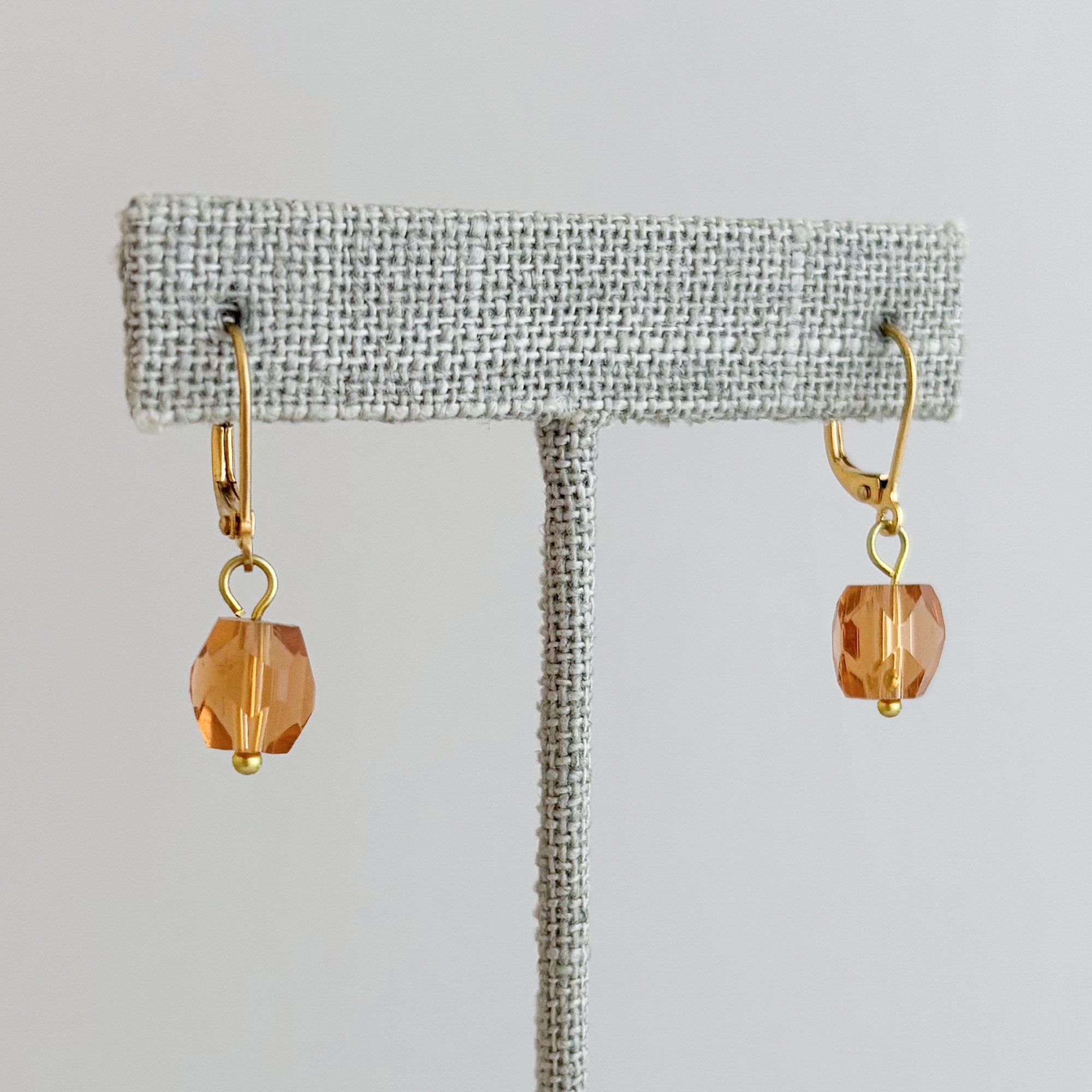 Pair of gold-tone drop earring with a faceted topaz-coloured crystal displayed on linen stand
