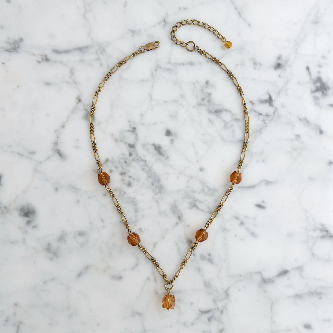 Model wearing a delicate gold-tone chain necklace with faceted amber-coloured crystals and a central drop