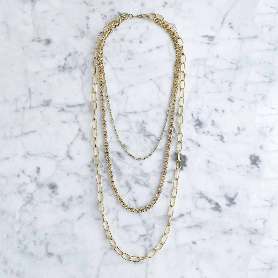 Model wearing a lightweight gold-tone necklace with three layered chains in fine, curb and elongated oval link styles
