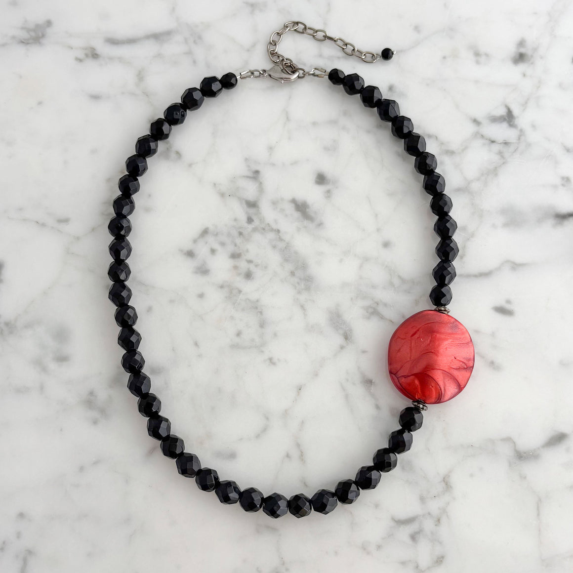Woman wearing a black faceted crystal bead necklace with a marbled red lucite accent