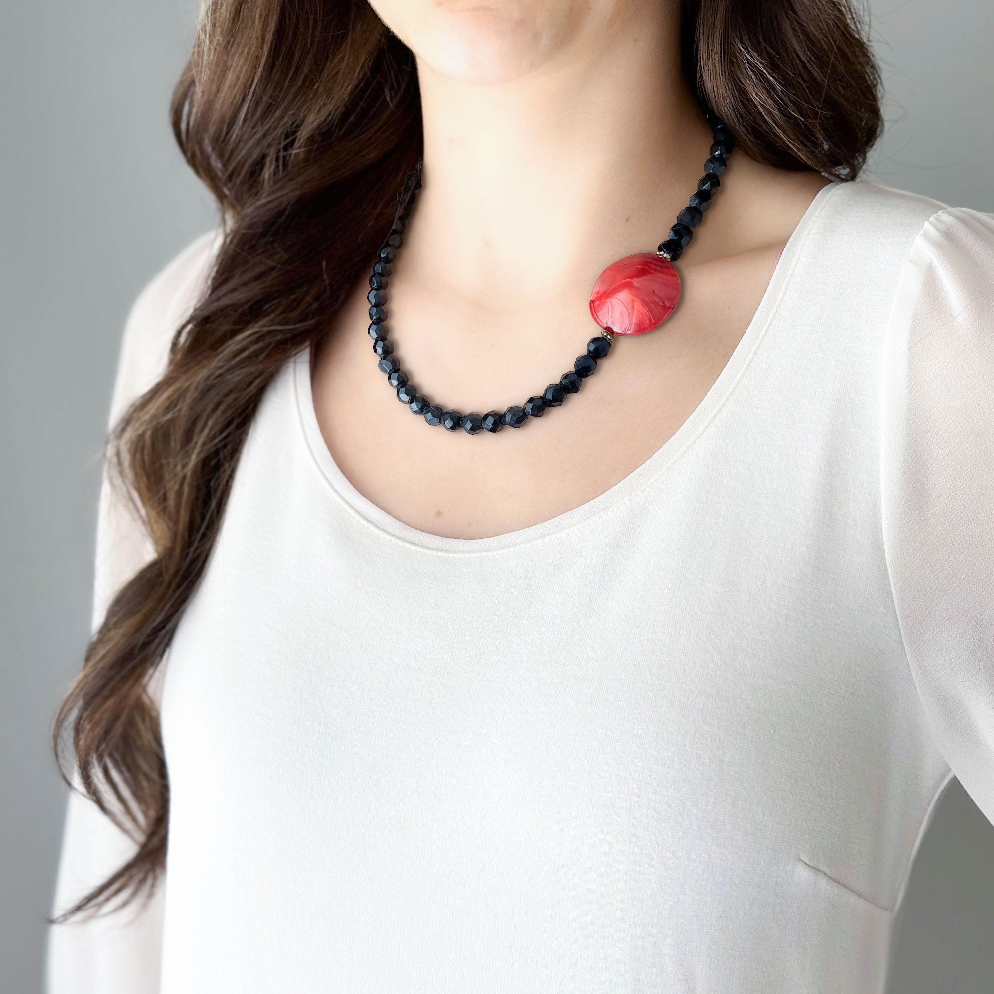 Woman wearing a black faceted crystal bead necklace with a marbled red lucite accent