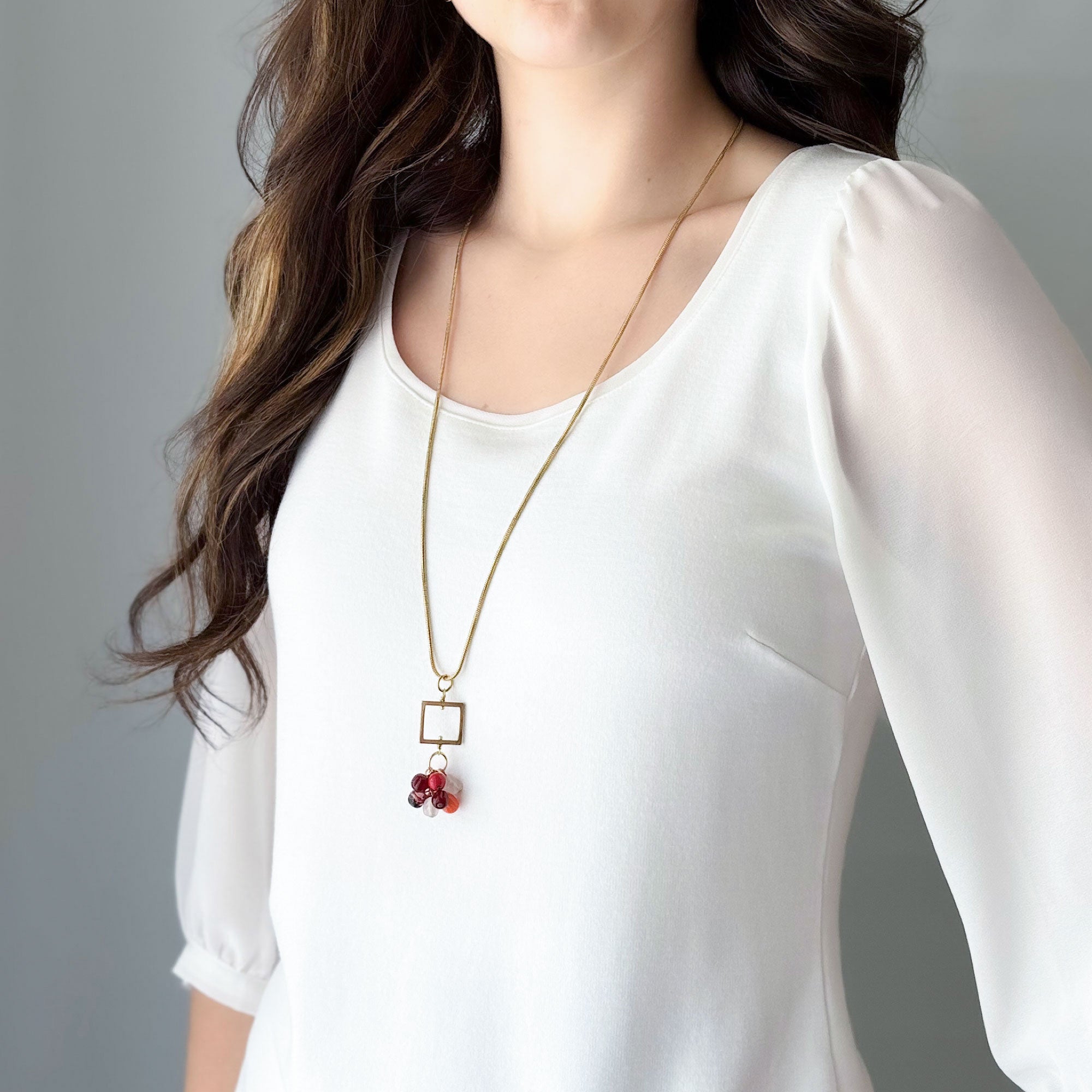 Woman wearing a long vintage glass bead cluster pendant necklace in orange, red and amethyst tones