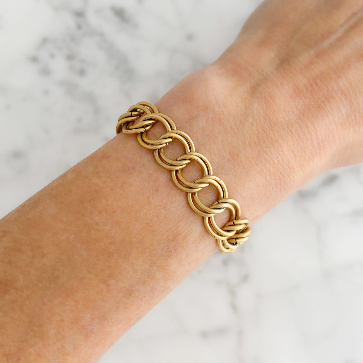 Vintage matte gold-tone double-link curb chain bracelet arranged on white marble