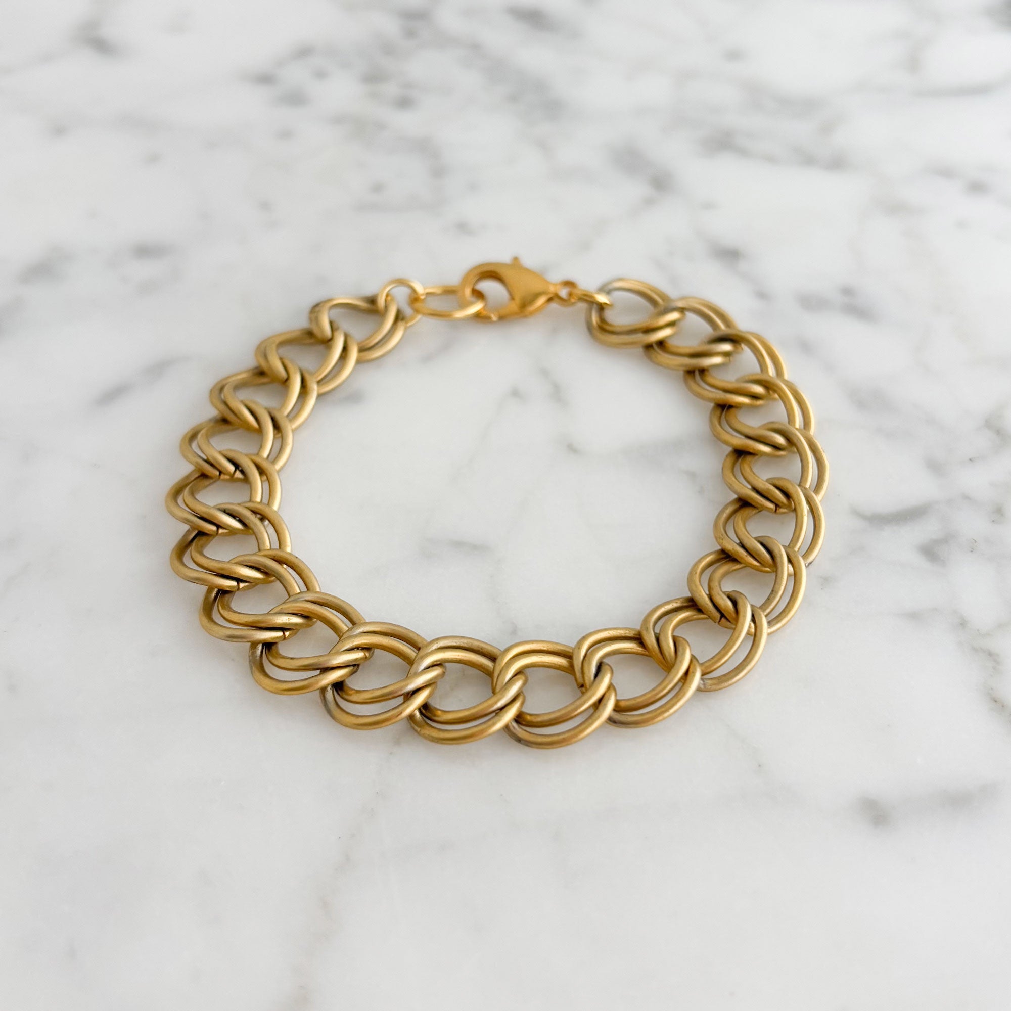 Vintage matte gold-tone double-link curb chain bracelet arranged on white marble