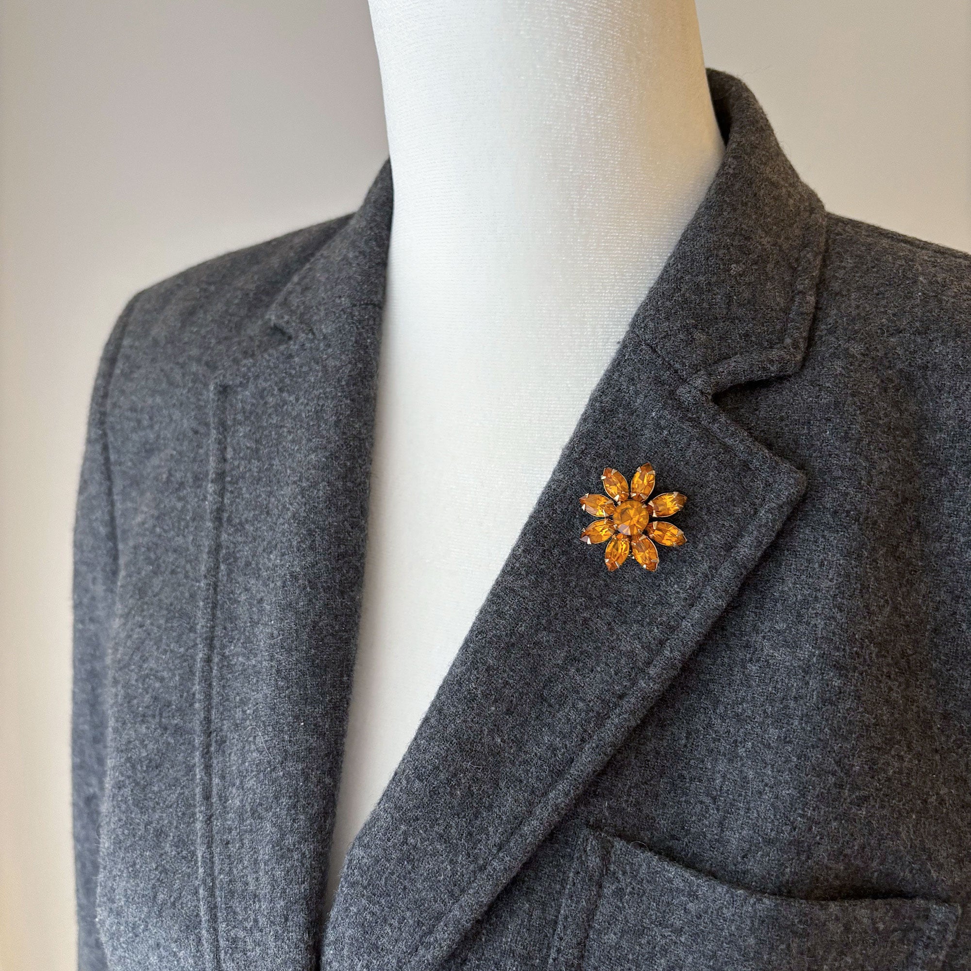 Vintage orange rhinestone floral brooch worn on the lapel of a grey blazer