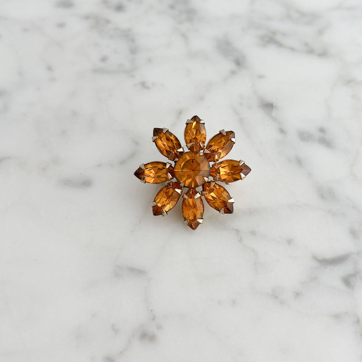 Vintage orange rhinestone floral brooch worn on the lapel of a grey blazer