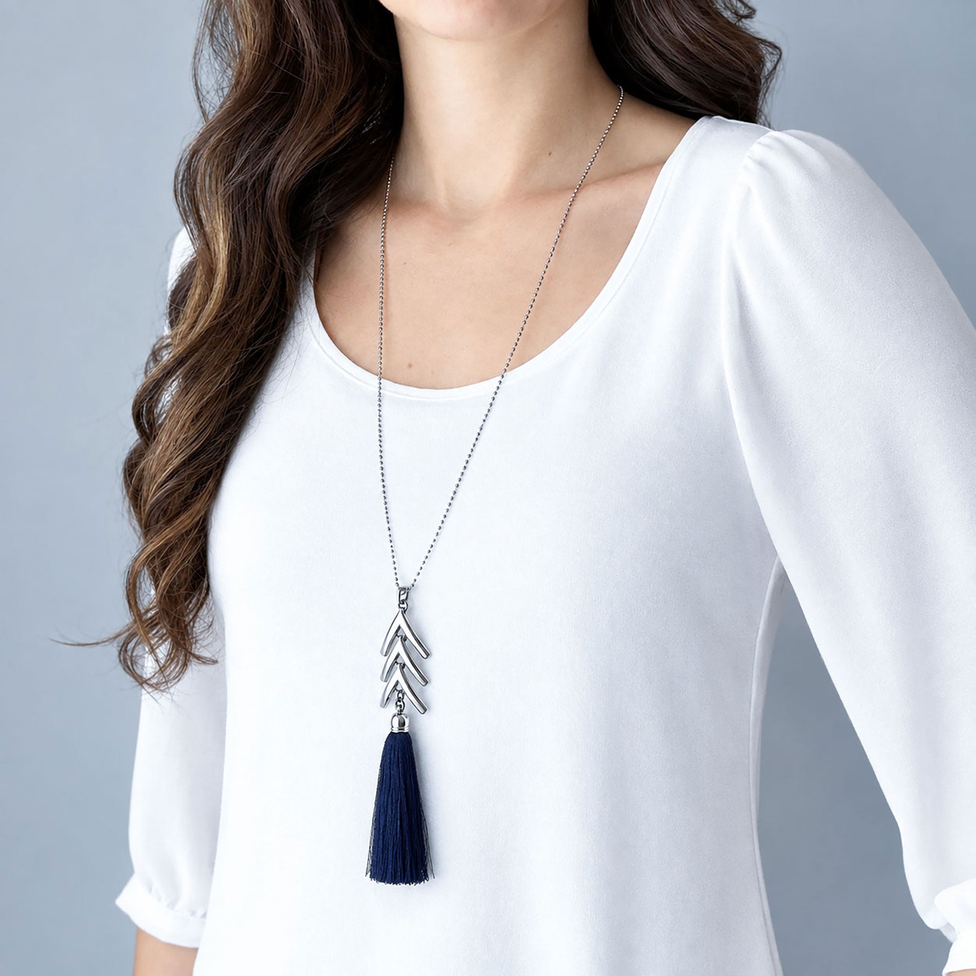 Woman wearing a long silver tone chevron necklace with a black silk tassel