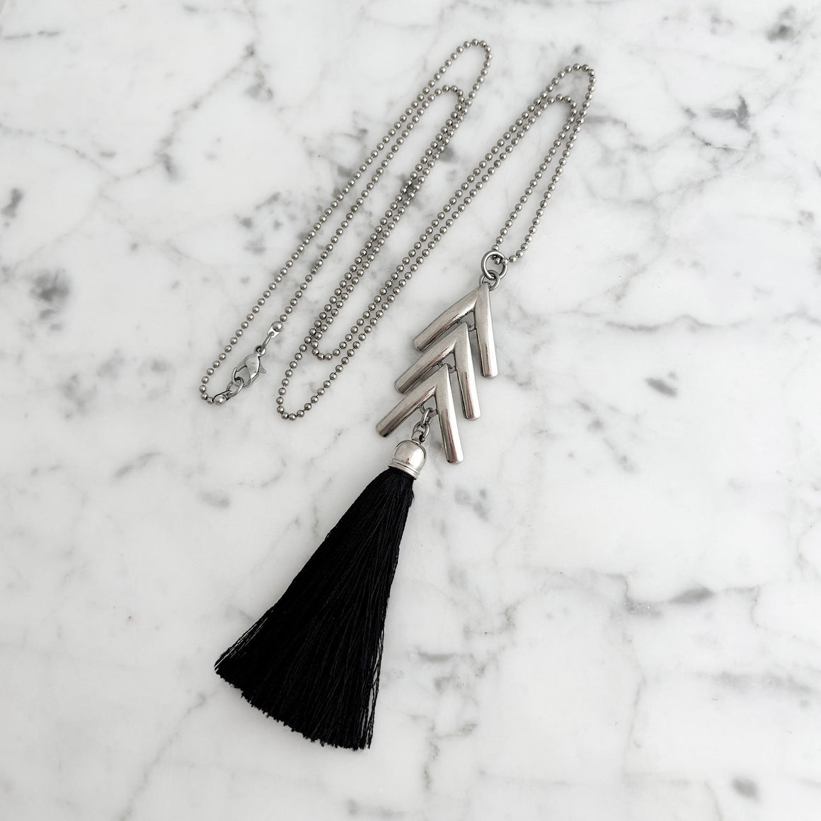 Woman wearing a long silver tone chevron necklace with a black silk tassel