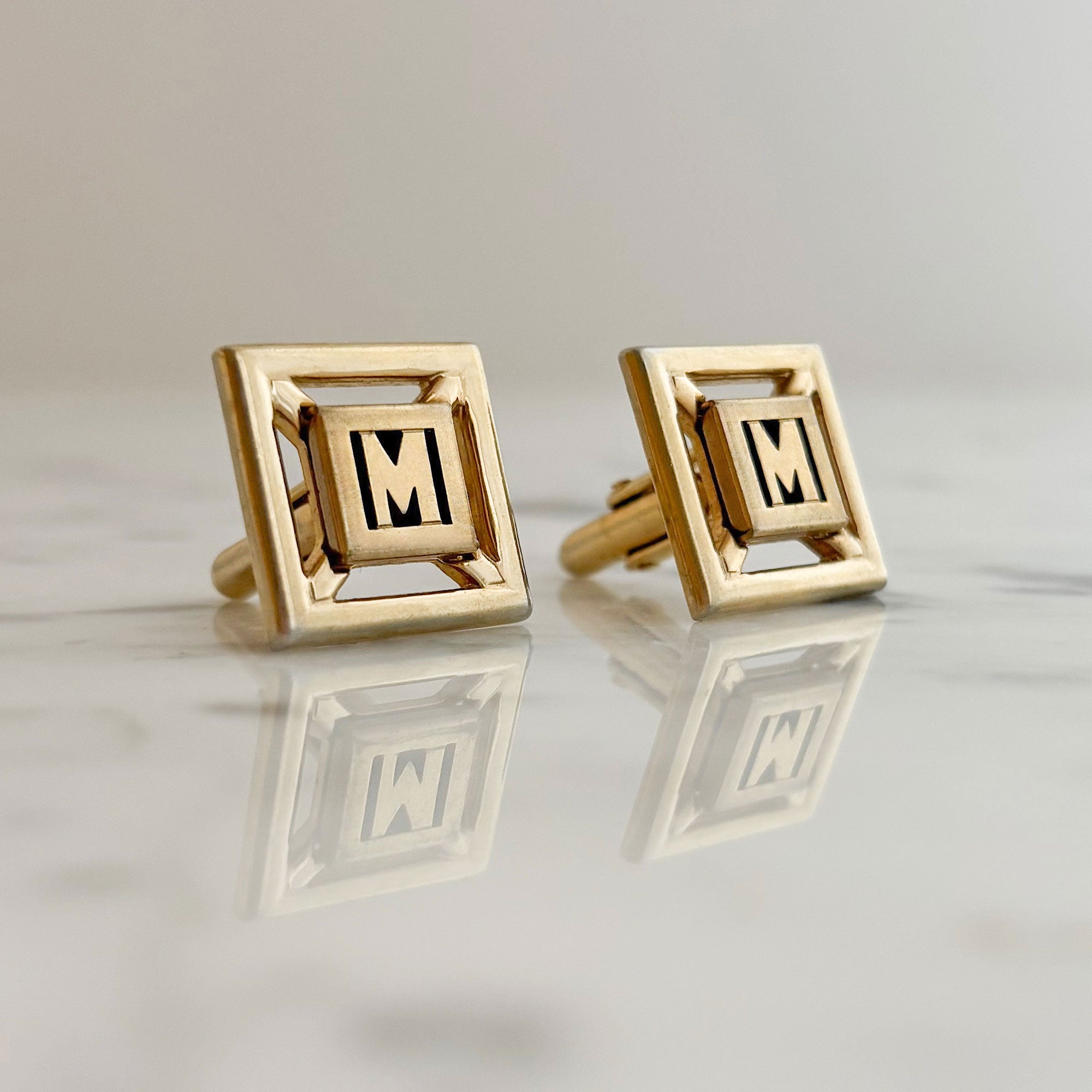 Vintage Swank gold-tone cufflinks with black enamel M monogram displayed on marble