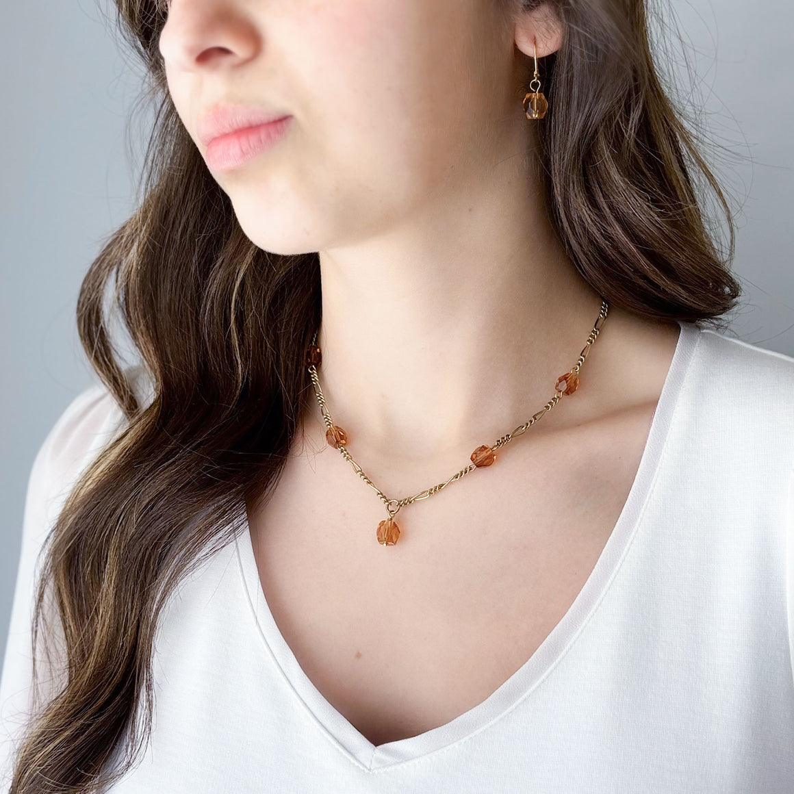 Pair of gold-tone drop earring with a faceted topaz-coloured crystal displayed on linen stand
