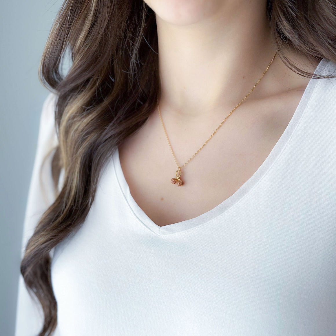 Close-up of a tiny gold-tone wishbone pendant with two topaz-coloured stardust beads on white marble